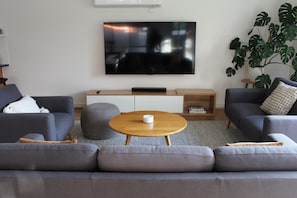 Una sala de estar moderna con un televisor de pantalla plana, sofás grises, una mesa de centro de madera y una planta grande.