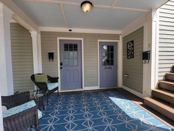 A covered porch with two doors, a blue patterned rug, and wicker furniture. - Modern Industrial Loft • Walkable Downtown Raleigh (Raleigh)