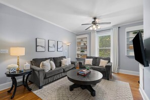 A living room with two grey sofas, a round coffee table, a ceiling fan, and a TV on the wall.