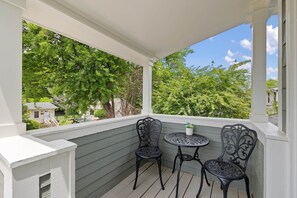 A covered porch with two ornate chairs and a small table, overlooking a green landscape. - Charming Studio Apt in Downtown Raleigh-Walkable location! (Raleigh)