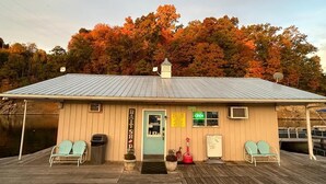 A wooden building with a sign reading "BATSHOP" and a green "OPEN" sign. There are two chairs outside and a dock extending into a body of water. - Rustic 2BR Fisherman’s Retreat on Douglas Lake! (Dandridge)