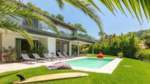 Una casa moderna con piscina, sillas de descanso y una tabla de surf.