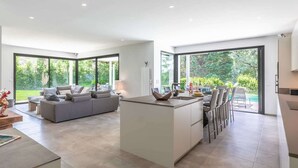 Una cocina moderna con una isla central, ventanas amplias y un comedor con sillas.