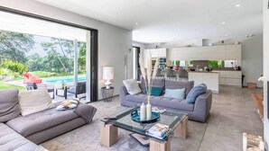 Un salón moderno con una mesa de centro de vidrio, sofás grises y vistas a una piscina y jardín.