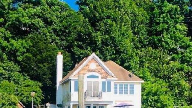 A house with a white exterior, a brown roof, and a balcony. It is located on stilts over water, surrounded by dense green trees. - Waterfront Studio Beach Cottage Wow Sunsets Walk to Village Shops Winery Brewery (Northport)