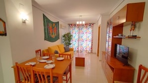 Un área de comedor con una mesa y sillas de madera, un sofá y un televisor sobre un mueble de madera.