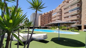 Zona de piscina con una gran escultura de roca, palmeras y un edificio de varios pisos al fondo.