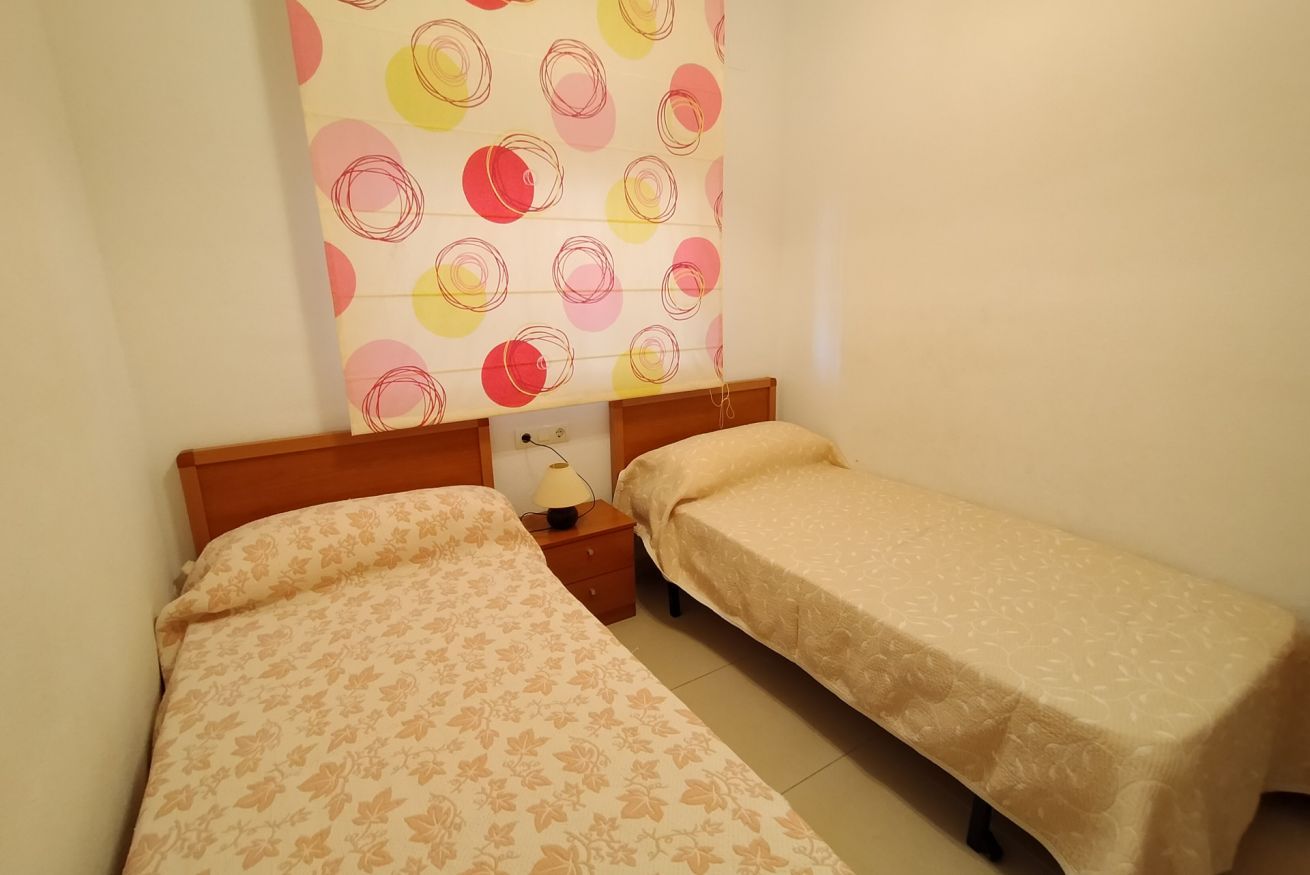 Ein Zimmer mit zwei Einzelbetten, einem Nachttisch mit Lampe und einer Wand mit einem Rundmuster.