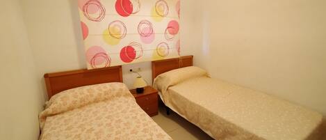 Una habitación con dos camas individuales, una mesita de noche con lámpara y una pared con diseño circular.