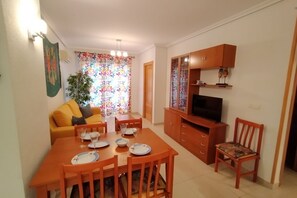 Ein Essbereich mit Holztisch und Stühlen, einer Couch, einem Fernseher und einem Schrank.