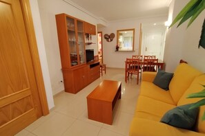 Ein Wohnzimmer mit gelbem Sofa, Holztisch, Esstisch mit Stühlen und einem Schrank mit Glastüren.