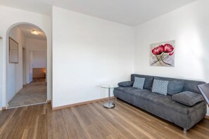 A modern living room with a grey sofa, a small glass table, and a painting of red flowers on the wall. - Apartment 'Viertelgraun' with Mountain View, Shared Terrace and Wi-Fi (Tramin an der Weinstraße)