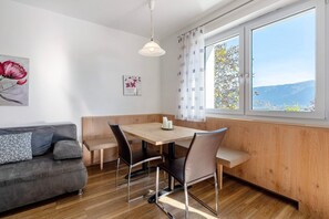 A dining area with a wooden table, four chairs, a bench, a sofa, and a large window with a view. - Apartment 'Viertelgraun' with Mountain View, Shared Terrace and Wi-Fi (Tramin an der Weinstraße)