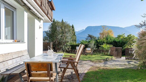 A patio with a table and chairs, a wooden bench, and a view of mountains.