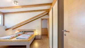A bedroom with a wooden ceiling, a bed with striped bedding, a bedside table with a lamp, and a wooden door.