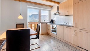A kitchen with wooden beams, a dining area with a table and chairs, and a view through a window.
