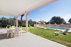 Eine überdachte Terrasse mit Pool, Sitzgelegenheiten im Freien und Blick auf die umliegende Landschaft.