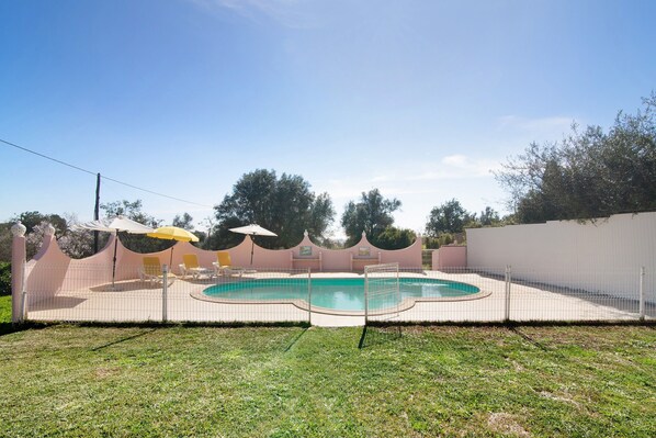 Ein Garten mit Swimmingpool, Zaun und einigen Liegestühlen.