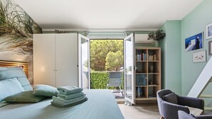 Ein Schlafzimmer mit Bett, Sessel, Bücherregal und Blick ins Grüne durch eine Glastür.