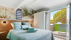 Ein Schlafzimmer mit Bett, Kissen, Nachttisch, Kleiderschrank und Blick ins Freie.