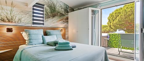 A bedroom with a bed, pillows, a bedside table, a wardrobe, and a view of the outdoors.