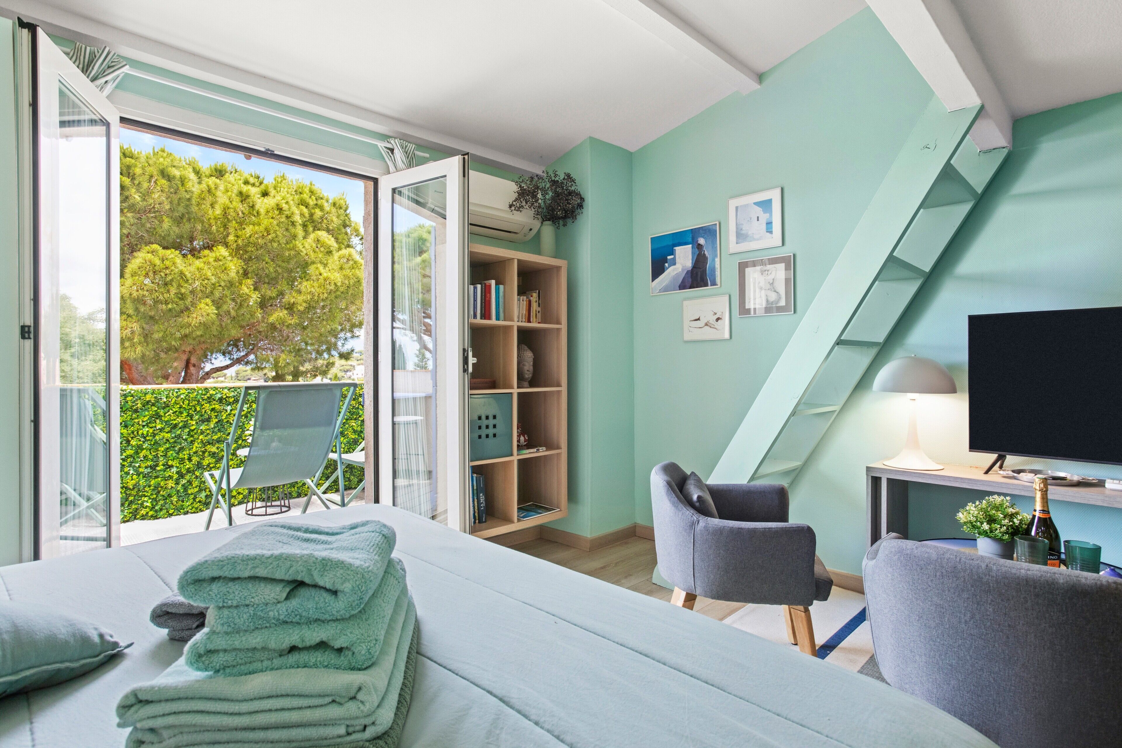Ein modernes Schlafzimmer mit Bett, Fernseher, Bücherregal und einem Balkon mit Blick auf Bäume.
