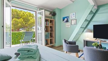Ein modernes Schlafzimmer mit Bett, Fernseher, Bücherregal und einem Balkon mit Blick auf Bäume.