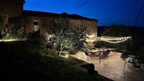 Un bâtiment en pierre doté d’un patio, d’un espace extérieur aménagé avec des sièges et de guirlandes lumineuses.