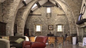 Une pièce aux murs de pierre, dotée d’un haut plafond voûté, d’une cheminée, d’une table à manger avec des chaises et d’un canapé.