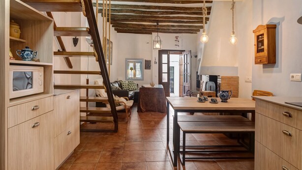 Ein rustikales Interieur mit freiliegenden Holzbalken, einer Treppe, einem Essbereich mit Tisch und Stühlen sowie einer Küche mit Schränken und einer Mikrowelle.