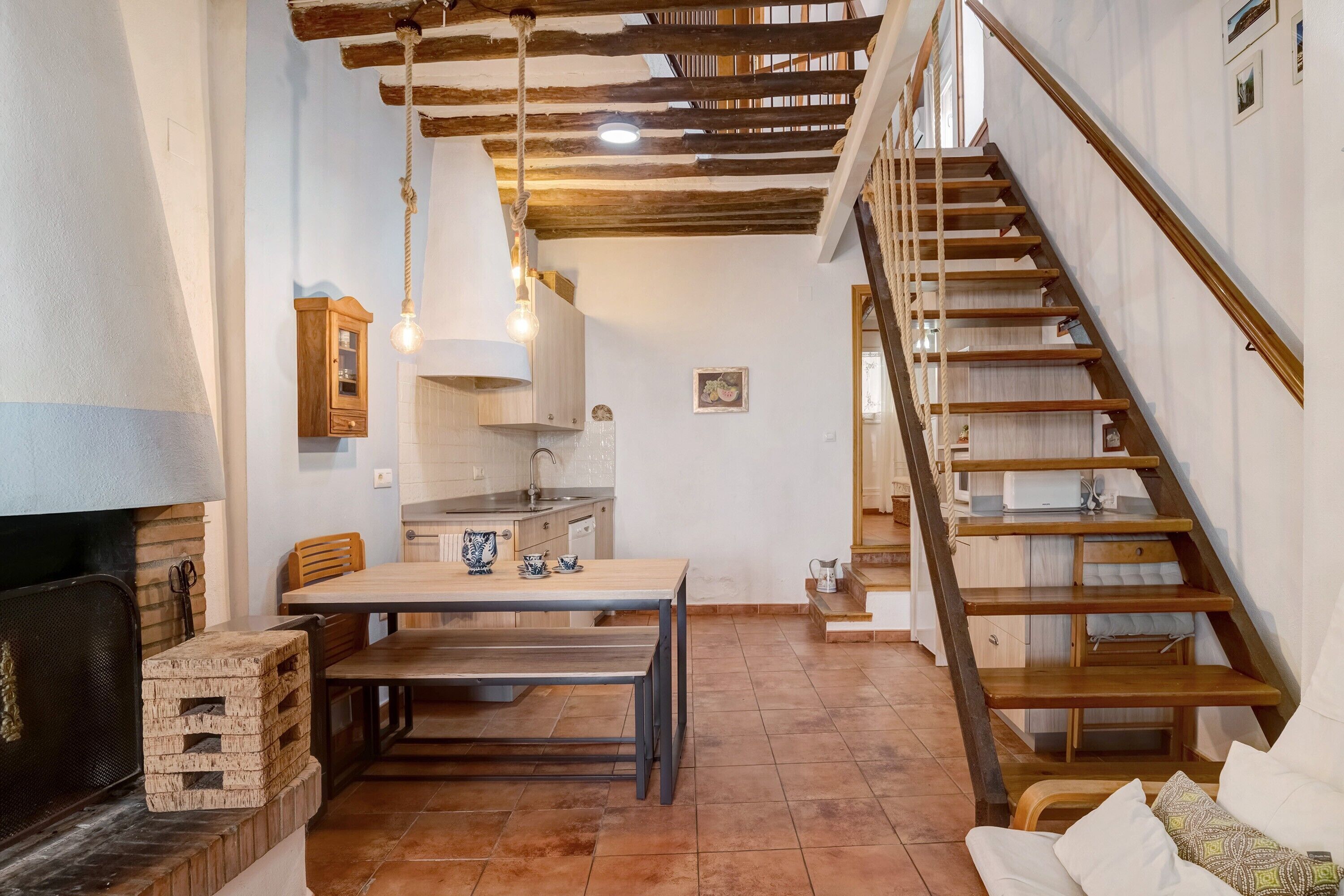 Una cocina con una mesa de comedor, una escalera de madera y una lámpara colgante.
