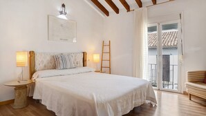 Ein Schlafzimmer mit Bett, Nachttischlampen, einer Leiter, einem Sessel und einem Balkon mit Ziegeldach.
