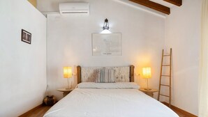 Ein Schlafzimmer mit einem Bett, zwei Nachttischlampen, einem gerahmten Kunstwerk, einer Leiter und einer Klimaanlage.