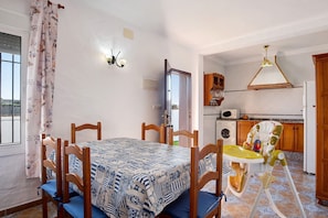 A dining area with a table and chairs, a baby high chair, a washing machine, and a kitchen area. - Holiday Home 'Las Calas De Roche' with Private Garden and Wi-Fi (Conil de frontera)