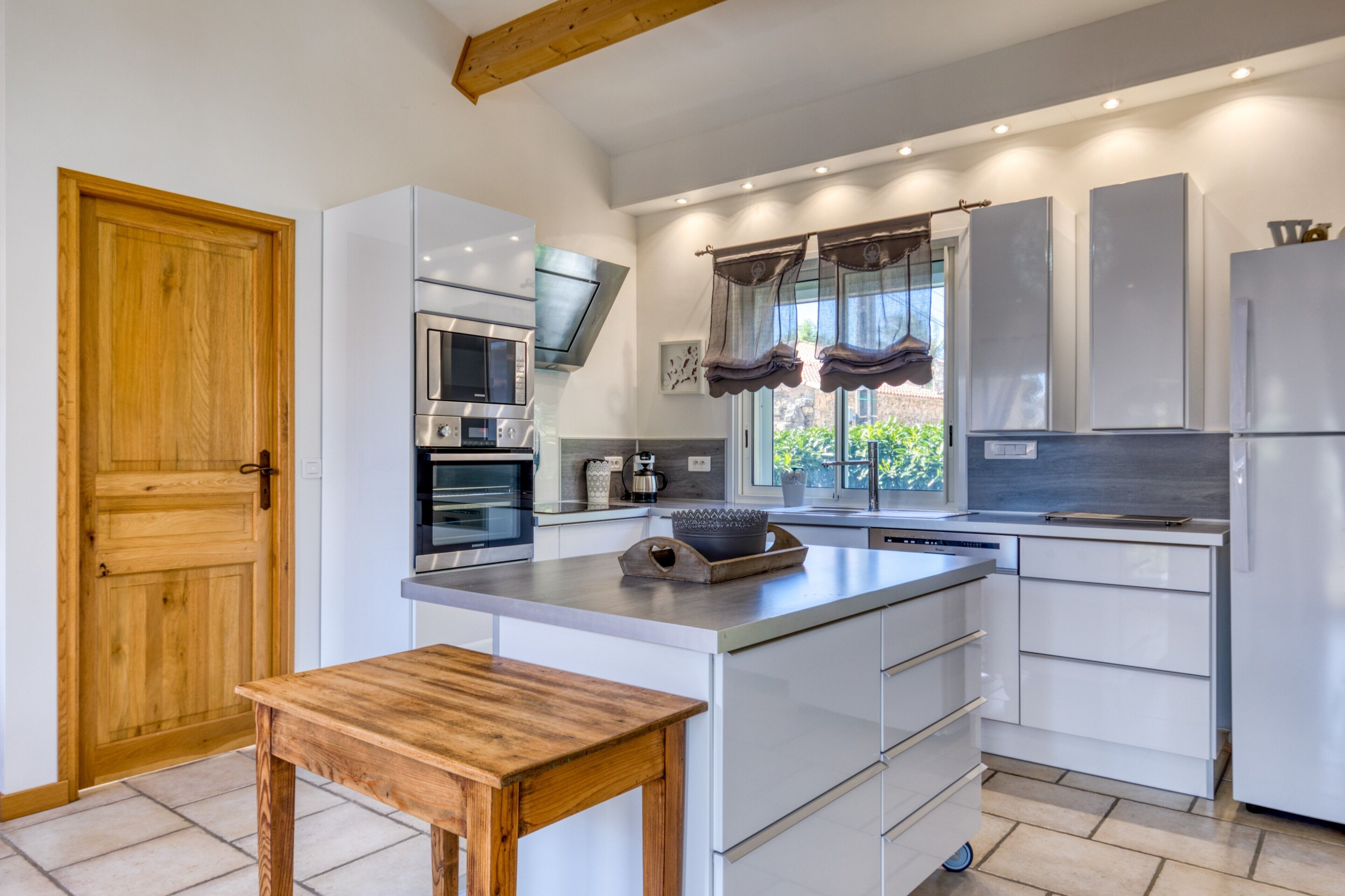 Une cuisine moderne avec des meubles blancs, une table en bois et un four encastré.