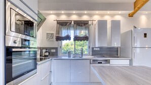 Een moderne keuken met inbouwapparatuur, een raam met gordijnen en een houten balk.