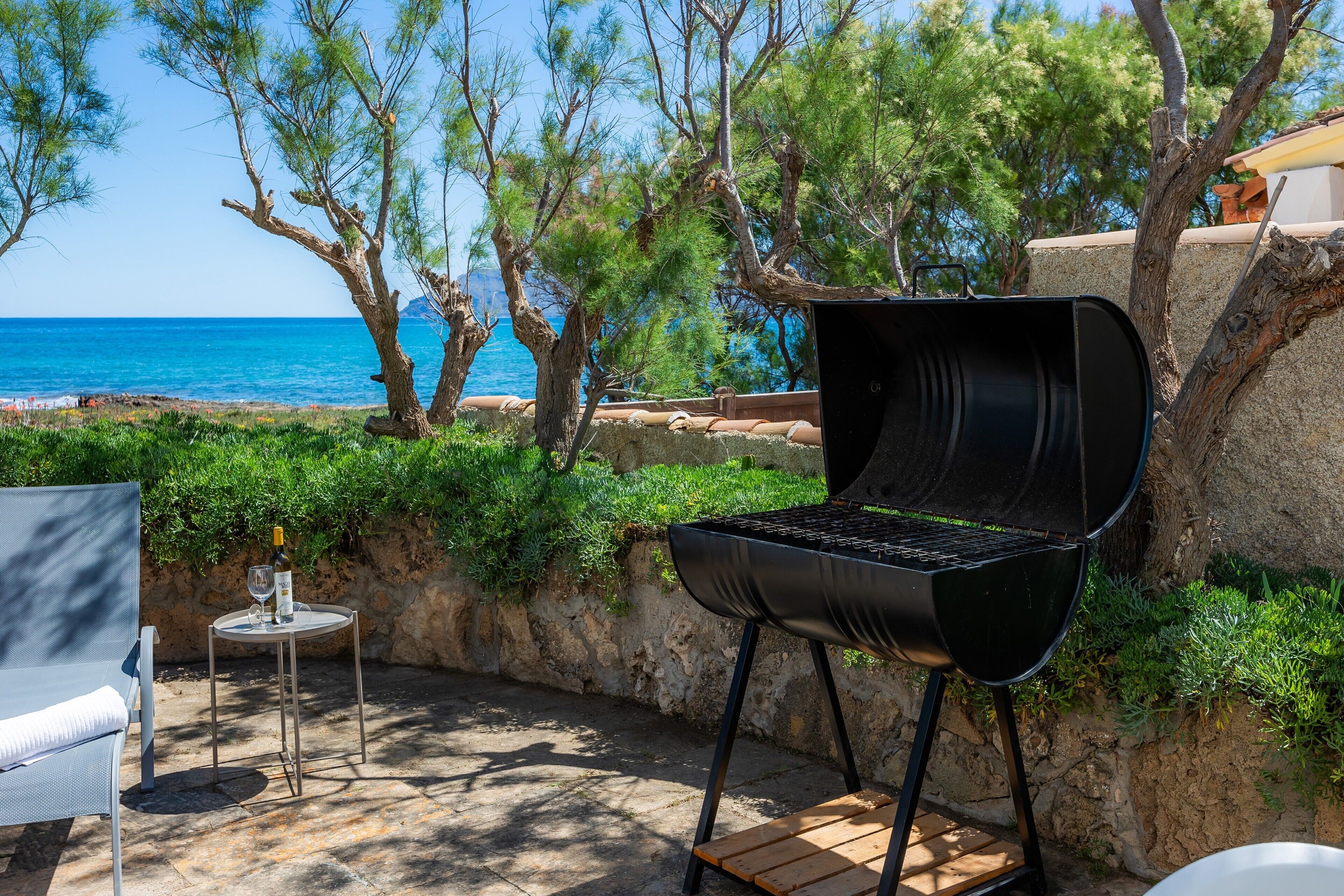 Une terrasse extérieure avec un barbecue, une table avec une bouteille et un verre, et une chaise.