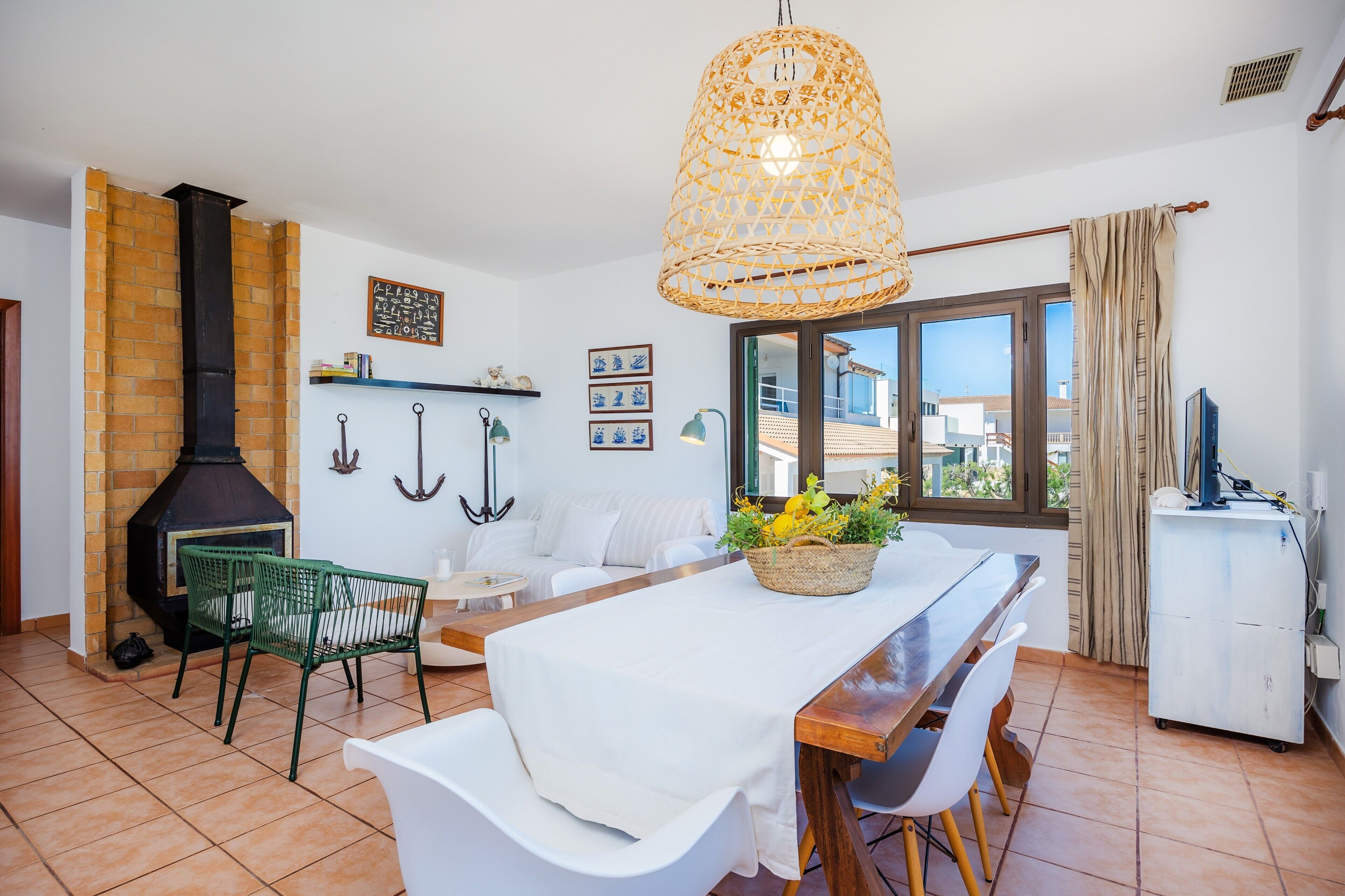 Un comedor con una mesa, sillas, una lámpara colgante, una chimenea de ladrillo y una ventana con cortinas.