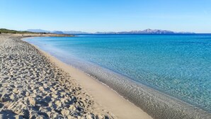 Une plage à l’eau d’un bleu limpide, bordée d’un rivage sablonneux, avec des montagnes qui se dessinent à l’horizon.
