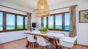 Un espace repas comprenant une table, des chaises, un luminaire suspendu et de grandes fenêtres offrant une vue sur la mer.