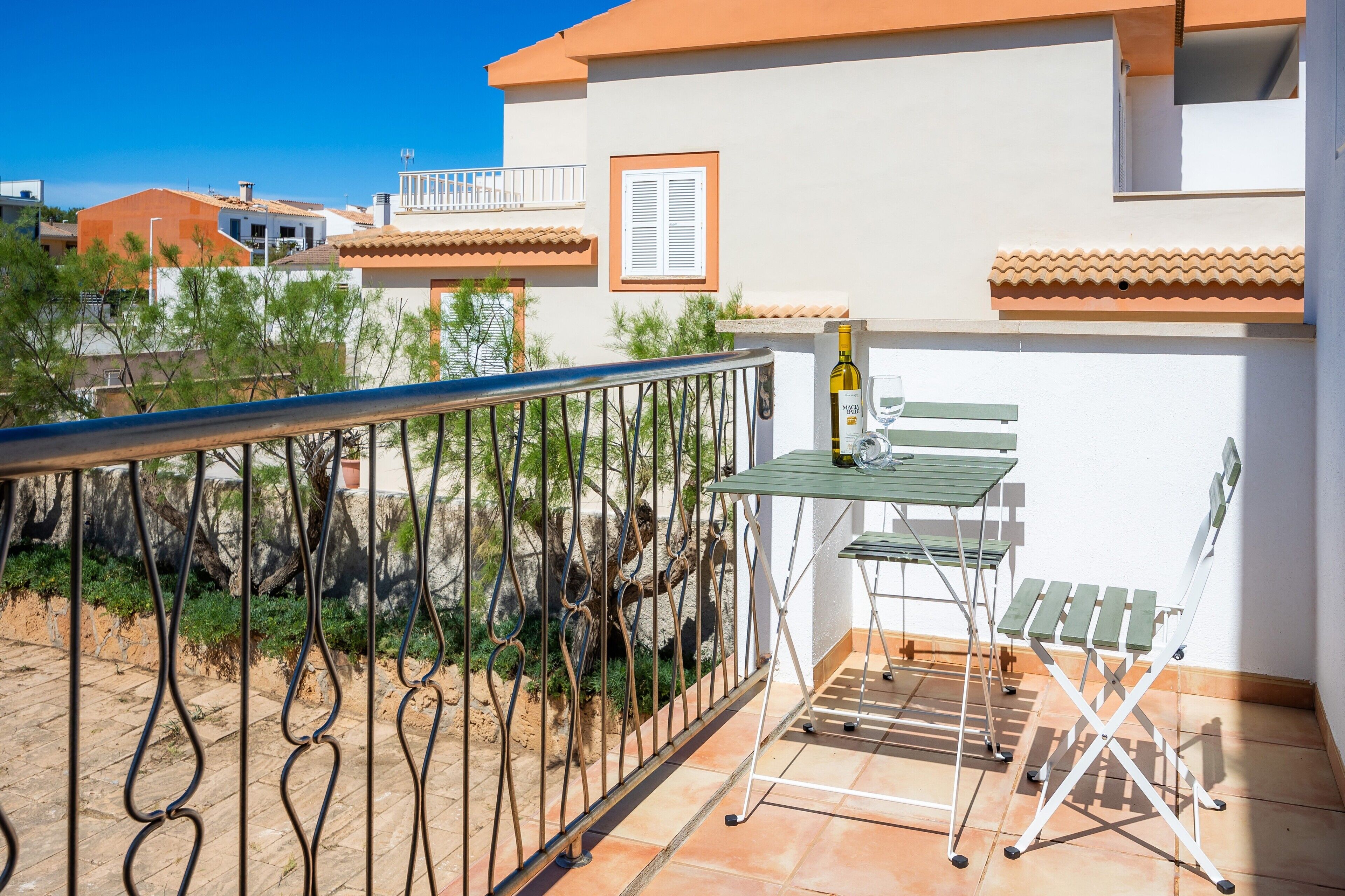 A balcony with a metal railing, a table with chairs, and a bottle of wine.