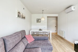 A modern living room with a gray sofa, a dining table with chairs, a pendant light, and a white air conditioner. - Apartment 'Georges' with Shared Terrace, Balcony and Air Conditioning (Roses)