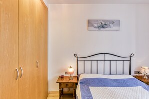 A bedroom with a bed, wooden wardrobe, bedside table with lamp, and a painting on the wall. - Apartment 'Georges' with Shared Terrace, Balcony and Air Conditioning (Roses)