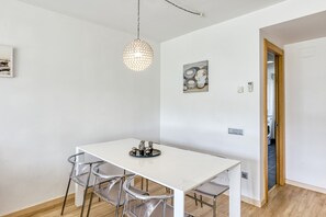 A dining area with a white table, clear chairs, a hanging light fixture, and a painting on the wall. - Apartment 'Georges' with Shared Terrace, Balcony and Air Conditioning (Roses)