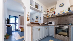 Een keuken met witte kastjes, een magnetron, een oven en een raam met een blauw gordijn.