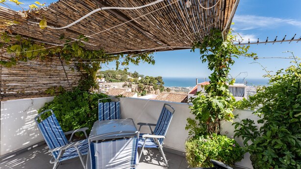 Een terras met een tafel en stoelen, een bamboe pergola en uitzicht op zee.