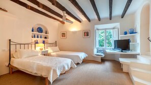 Une chambre avec deux lits, un bureau avec un ordinateur, une télévision et une fenêtre donnant sur un paysage verdoyant.