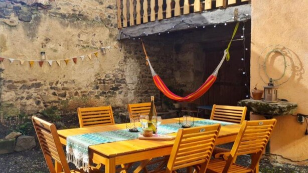 Un espace de restauration extérieur de style rustique, avec un mur en pierre, une table en bois et des chaises.