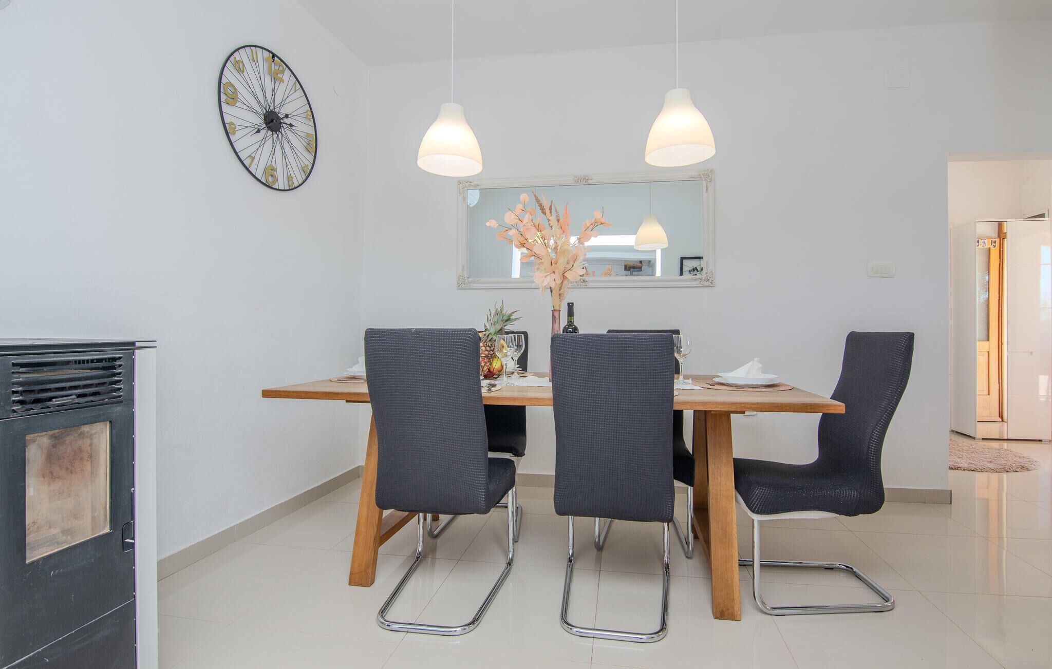 A dining area with a wooden table, four black chairs, a clock, and pendant lights.