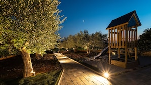 A nighttime outdoor area with a paved walkway, trees, and a wooden play structure. - Beautiful home in Debeljak (Debeljak)
